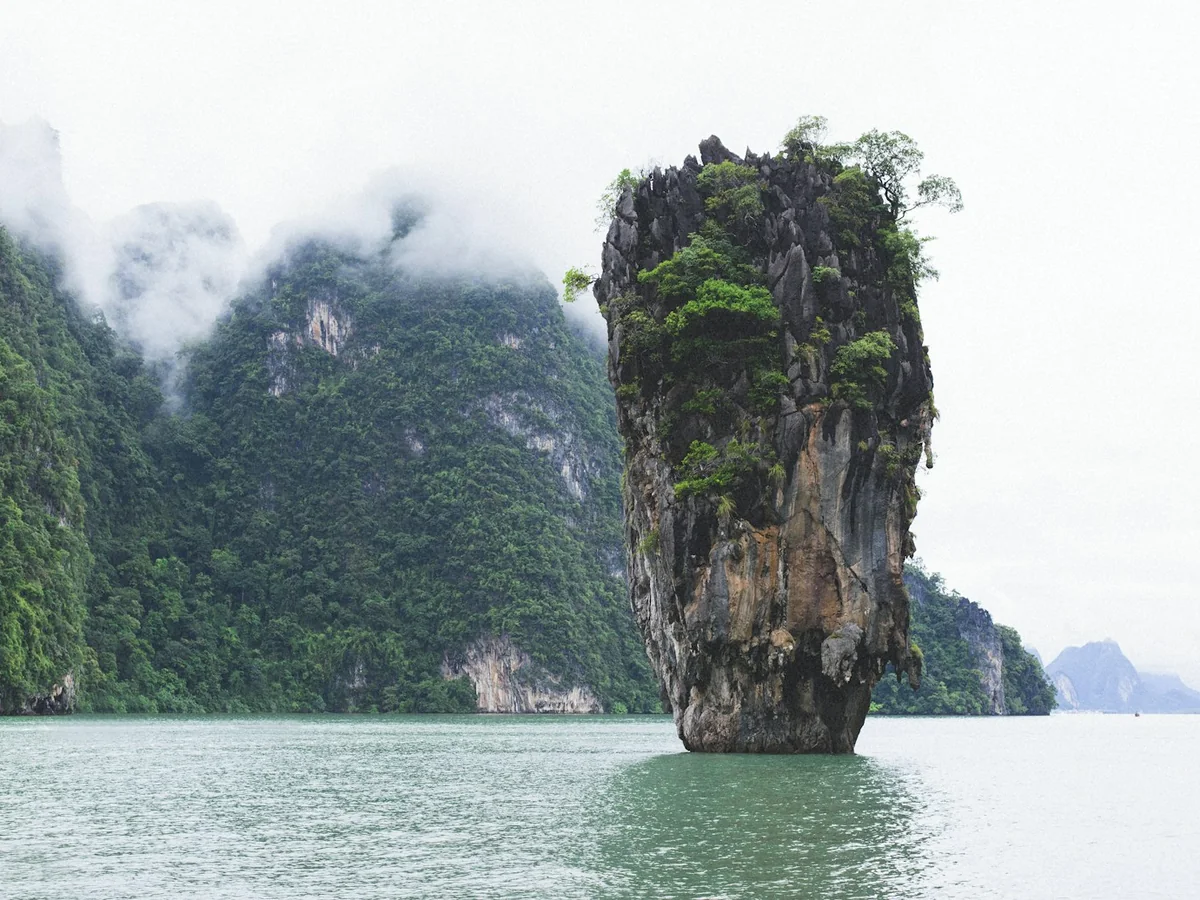 Ko Tapu rising beside the forested cliffs of Khao Phing Kan under low cloud